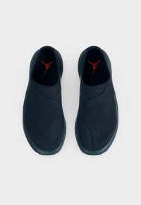 Ζευγάρι μαύρα αθλητικά παπούτσια τύπου slip-on με κόκκινο λογότυπο εσωτερικά, φωτογραφημένα από πάνω σε λευκό φόντο.