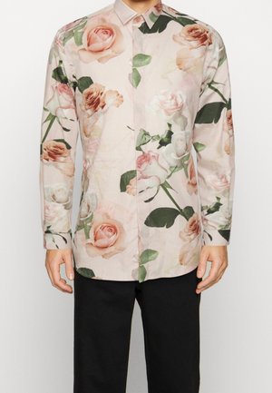 Chemise florale avec une base rose clair et de grands motifs de roses dans des teintes douces, manches longues, col boutonné et coupe décontractée.