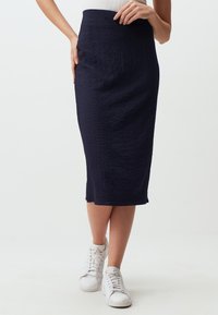 Gonna midi blu navy con finitura texturizzata, vita alta e spacchi laterali. Abbinata a scarpe da ginnastica bianche per un look casual.