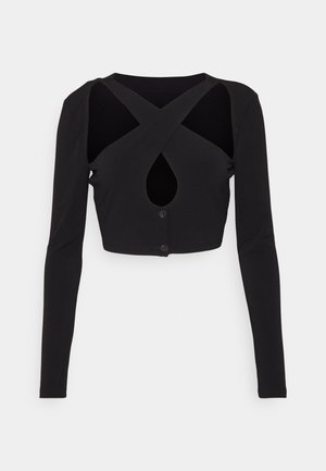 Haut court noir à manches longues en tissu doux, présentant un design croisé avec un détail en forme de goutte d'eau et une fermeture à bouton à l'avant.