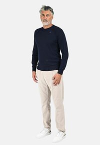 Pullover blu marine a maglia, collo rotondo, polsini e orlo a coste; abbinato a pantaloni in velluto a coste beige chiaro e sneakers bianche con dettagli neri.
