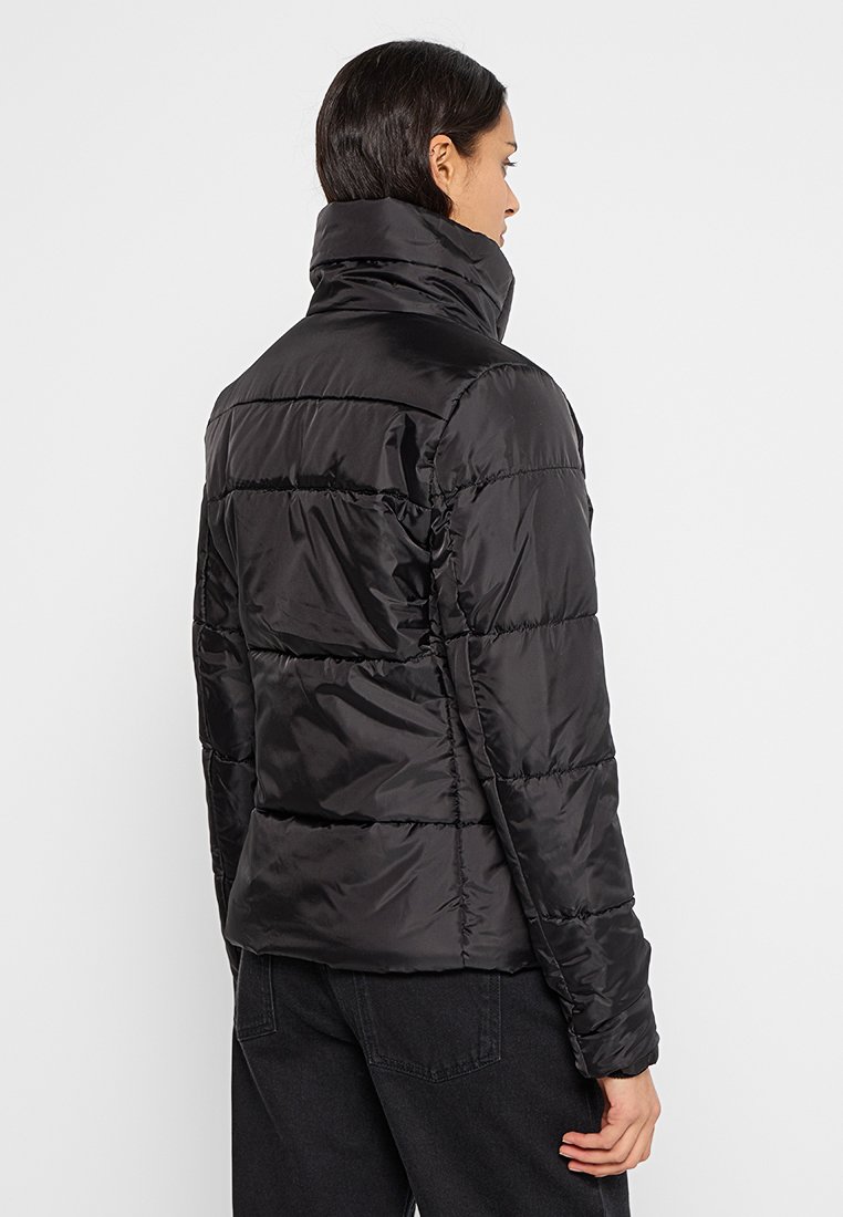 Chaqueta de plumas negra con cuello alto, que presenta secciones acolchadas y una textura suave y brillante. La vista trasera muestra una silueta ajustada y puños.