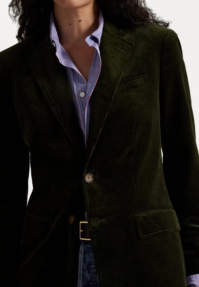 Dark green corduroy blazer with notched lapels, a single button closure, and a chest pocket, layered over a blue striped shirt.