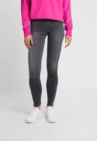 Jeans ajustados en denim gris oscuro, con una cintura de altura media y un leve desgaste, combinados con zapatillas blancas y un sudadera rosa.
