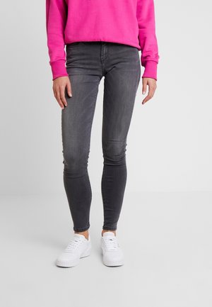 Jeans ajustados en denim gris oscuro, con una cintura de altura media y un leve desgaste, combinados con zapatillas blancas y un sudadera rosa.