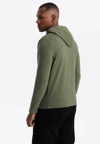 Felpa verde oliva con una silhouette aderente, dotata di cappuccio, maniche lunghe e polsini a costine, abbinata a pantaloni cargo neri.