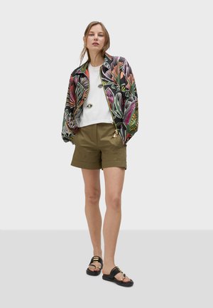 Veste bomber colorée et à motifs avec un design de feuilles de palmier; haut blanc; shorts vert olive; sandales noires avec des accents de sangle.