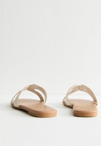 Platte sandalen met een neutraal gekleurde leren zool, voorzien van een minimalistisch ontwerp met twee gebogen banden en subtiele gouden accenten.