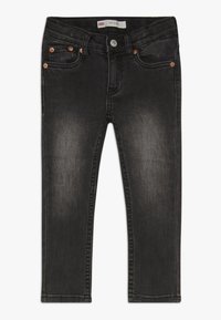 Jeans de mezclilla negra de corte ajustado, con herrajes de cobre, cinco bolsillos y detalles desgastados. La tela tiene un ligero estiramiento.