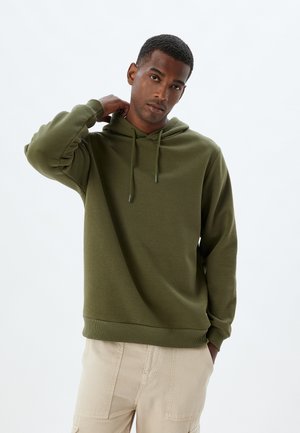 Olive green hoodie made of textured fabric; features a drawstring hood and ribbed cuffs. Worn with light-colored cargo pants.