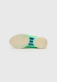 Sola di scarpa sportiva verde con una base in gomma testurizzata di colore crema, caratterizzata da una striscia d'accento blu e una parte superiore liscia e lucida.