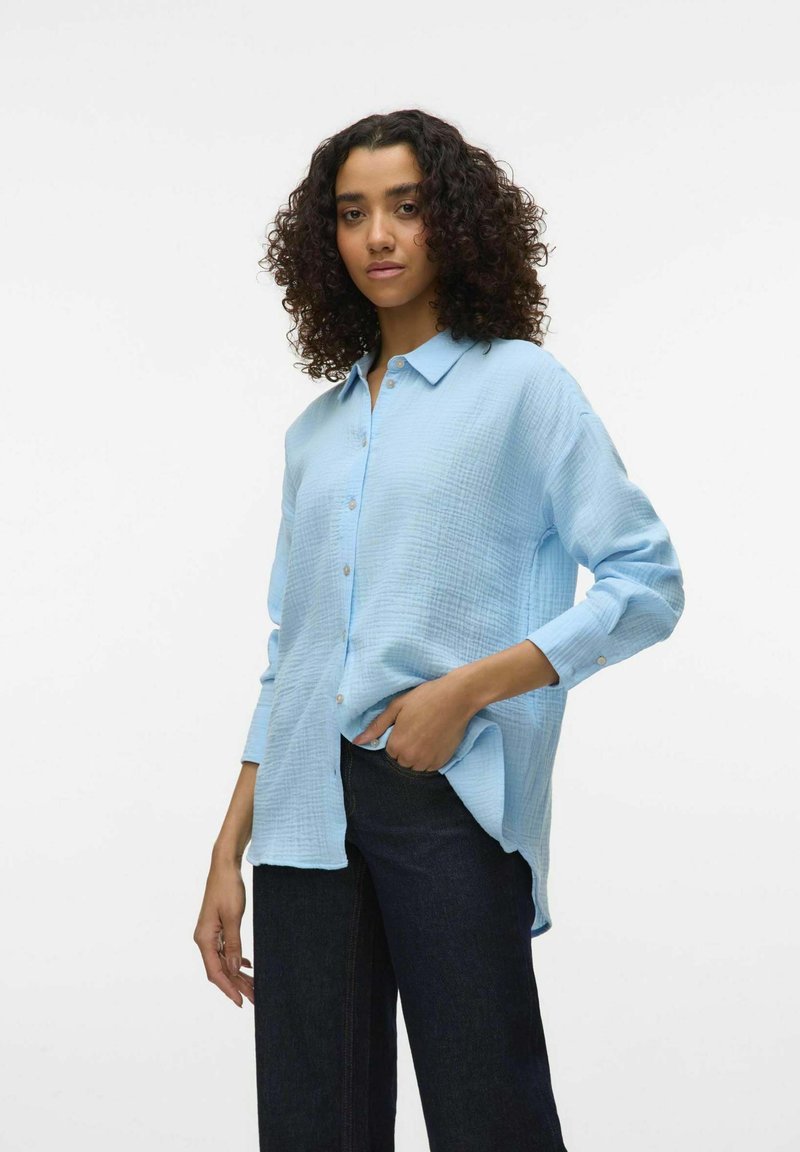 Light blue button-up shirt made of textured fabric, featuring a collar, long sleeves, and a relaxed fit, paired with dark jeans.