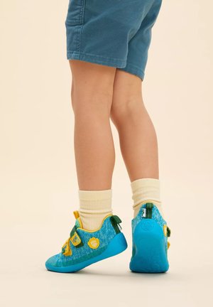 Blaue und gelbe Kinderschuhe mit einem strukturierten Stoffobermaterial, Riemendetails und einer Gummisohle, kombiniert mit cremefarbenen Socken.