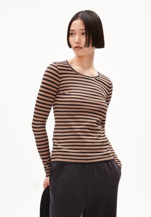 Maglietta a maniche lunghe a righe color beige e blu scuro, con scollatura rotonda e design aderente. Realizzata in tessuto morbido, abbinata a pantaloni jogger scuri.