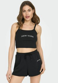 Svart cropped tank topp med teksten "NEW YORK" i hvitt. Kombinert med svarte shorts med snøring i livet som har samme tekst i hvitt. Enkelt, avslappet design.