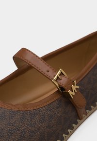 Καφέ δερμάτινο επίπεδο παπούτσι με ανάγλυφο σχέδιο, διαθέτει καφέ λουράκι και χρυσή αγκράφα με λεπτομέρεια λογότυπου MK.