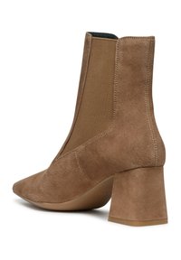 Stivale ankle in suede color beige con punta appuntita e pannello elastico laterale. Tacco a blocco e texture liscia con cuciture visibili e un design minimalista.