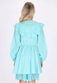 Rochie albastră deschisă cu guler volanat, mâneci lungi și puff, talie elastică și tiv cu dantelă. Fabricată dintr-un material neted cu o textură delicată.