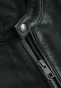 Zwarte leren jas met een metalen ritssluiting, drukknoopsluiting en een getextureerd oppervlak. Opvallende stiksels langs de randen.