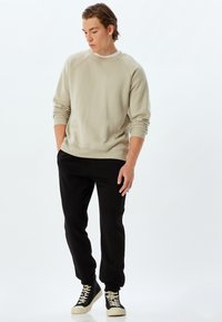 Lys beige sweatshirth med rund hals og ribbede manchetter, kombineret med sorte tætsiddende sweatpants og sorte højhælede sneakers.