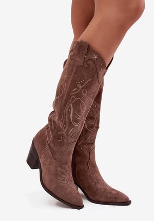 Bottes de cowboy en daim marron avec des pointes et un talon moyen. Présentent des coutures et des embellissements complexes, mettant en valeur un design décoratif.