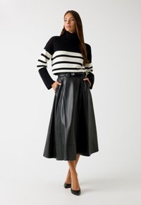 Gonna midi in pelle nera con design svasato e tasche, abbinata a un maglione a righe bianco e nero. Accento con una semplice cintura con fibbia.