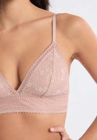 Spitzen-Bralette in zartem Rosa, mit dreieckiger Form, verstellbaren Trägern, gezackten Kanten und floralen Mustern für zusätzliche Details.