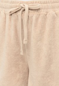 Short beige en tissu éponge avec ceinture élastique et cordon noué à l'avant.