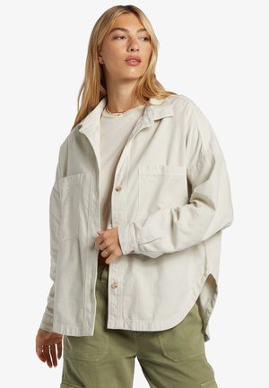 Light beige oversized jacket made of textured fabric, featuring two front pockets, button closures, and a curved hemline.