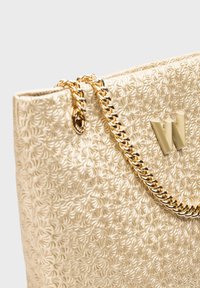 Sac fourre-tout texturé doré avec motif floral en relief, doté d'une anse en chaîne dorée et d'un accent logo à l'avant.