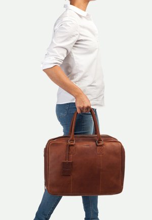 Sac à dos en cuir marron pour ordinateur portable avec double poignées, fermeture éclair et étiquette de bagage. Surface texturée et design robuste pour plus de fonctionnalité.