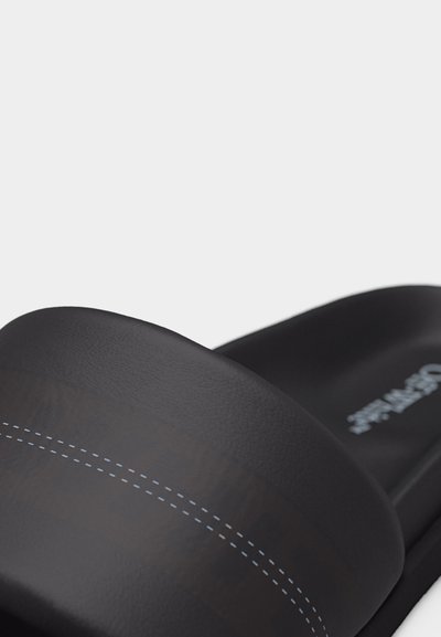 Μαύρο σανδάλι με φαρδιά λωρίδα και λευκές ραφές πάνω σε σκέτο φόντο.