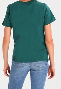 Grøn bomulds-t-shirt med korte ærmer, rund halsudskæring og lige kant. Båret med lyseblå jeans med baglommer.