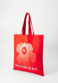 Piros vászontáska, nagy fehér virág grafikával, alján a "marimekko" felirattal vastag fehér betűkkel. Két vállpánttal.