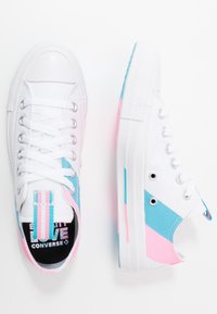 Zapatillas de lona blancas con acentos azules y rosas, punta redondeada, seis ojales y una lengüeta a rayas. Logo negro en la plantilla.