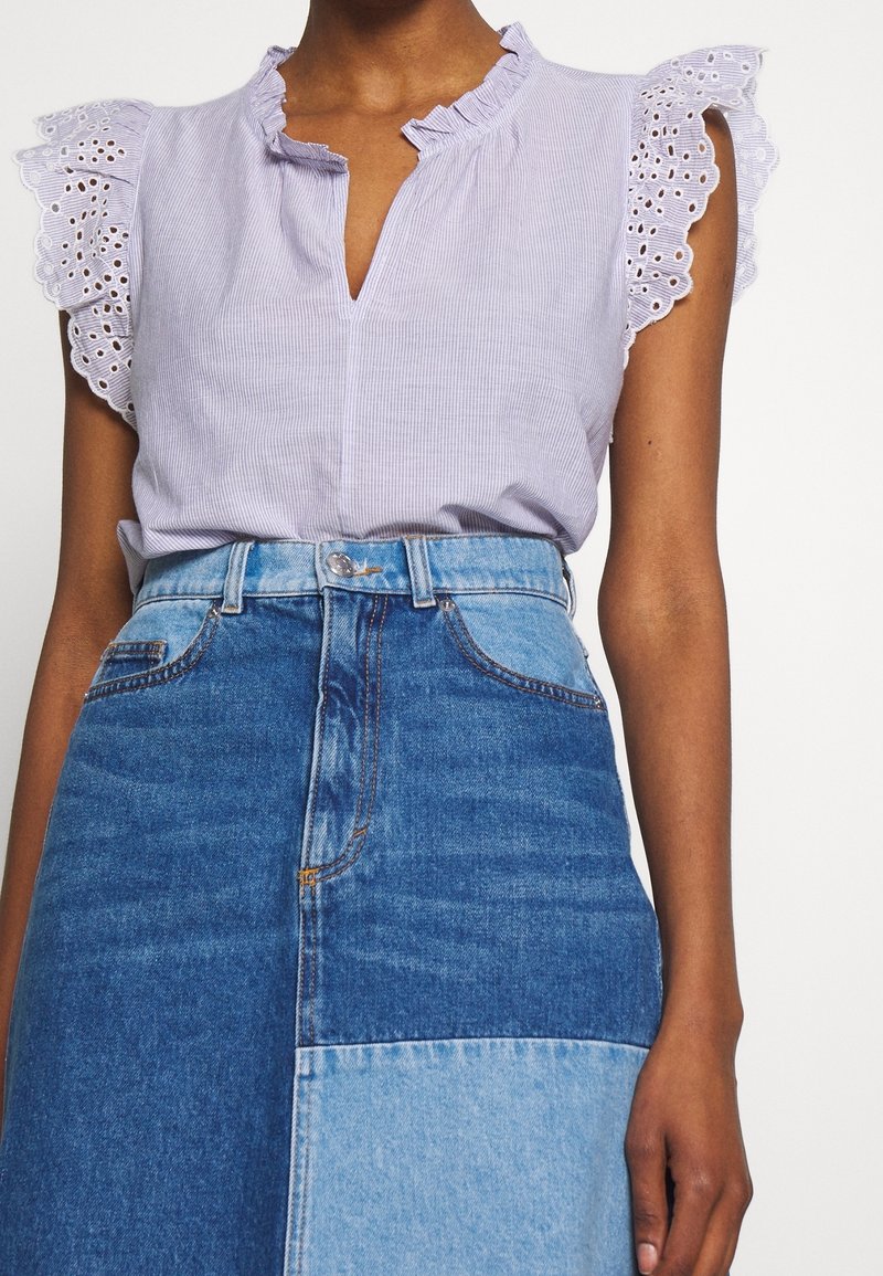 Vaaleanvioletti raidallinen pusero, jossa on röyhelökaulus ja silmäkuvioiset pitsiset hupunolkahihat, yhdistetty tumman- ja vaaleansiniseen pilkulliseen farkkuhameeseen.