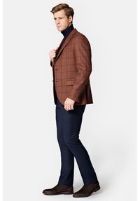 Brązowa marynarka w kratę o dopasowanym kroju, noszona na ciemnym golfie, zestawiona z ciemnoniebieskimi spodniami eleganckimi i brązowymi butami.