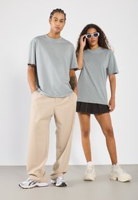 Šedé oversized trička, béžové kalhoty širokého střihu a černá džínová sukně. Jedna dvojice má na sobě bílé chunky tenisky, druhá šedé sportovní boty.