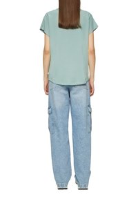 Lichtgroene, korte mouwen top met een ronde zoom, gecombineerd met lichtblauwe, losse cargobroek met zijzakken en een vervaagde textuur.