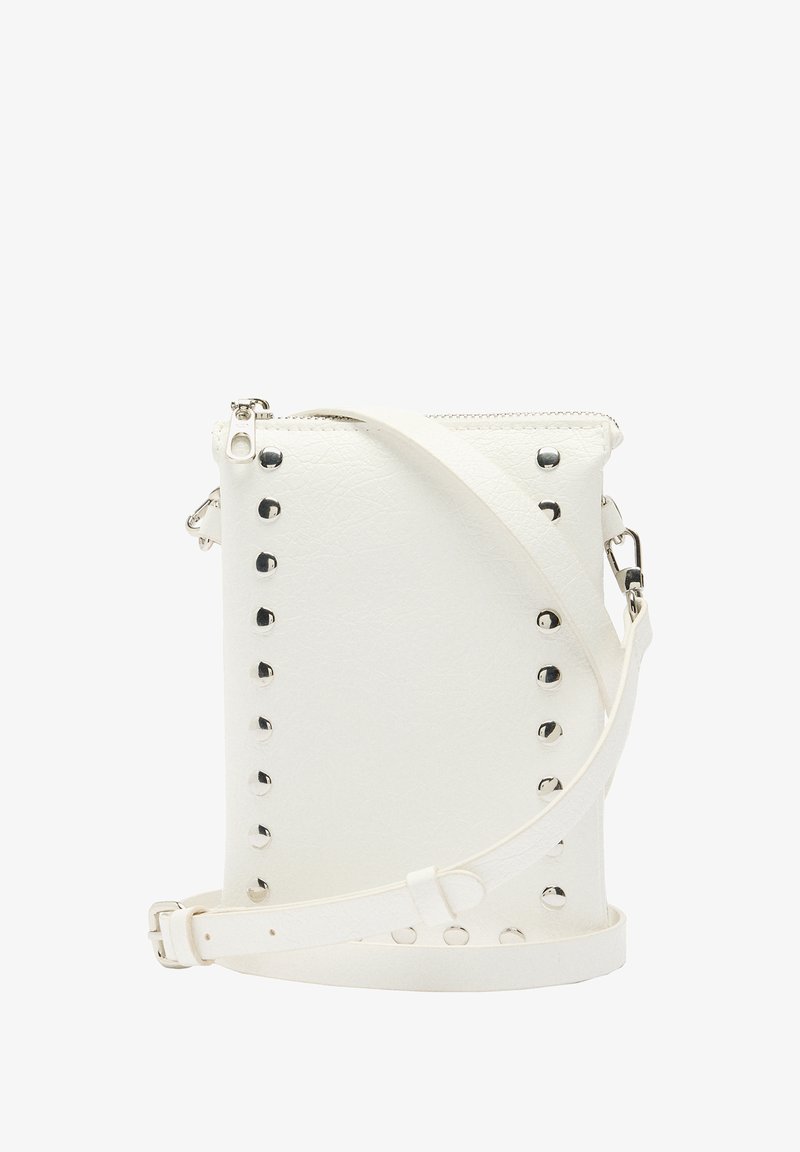 Biała torebka typu crossbody z sztucznej skóry, z srebrnymi ćwiekami po bokach, regulowanym paskiem i zamkiem błyskawicznym u góry. Gładka faktura.