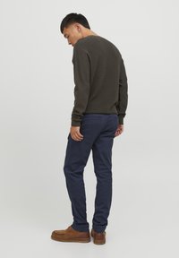 Dunkelgrüner strukturierter Strickpullover, marineblaue Hose und braune Schuhe. Das Outfit zeichnet sich durch eine lockere Passform und ein schlichtes Design ohne sichtbare Muster aus.