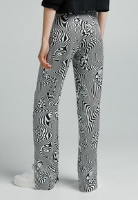 Svartvita mönstrade byxor med ett flödande mönster, prydda med svängar och blommiga detaljer; tillverkade av lättviktsmaterial, raka ben.