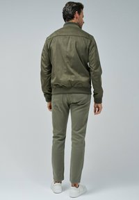 Olivno zeleni bomber jakna z gladko teksturo, rebrastimi manšetami in prilegajočimi hlačami v isti barvi, dopolnjena z belimi supergami.