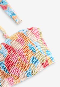 Bunt smockiertes Bandeau-Bikinitop mit verstellbaren dünnen Trägern mit einem mehrfarbigen Blumen- und geometrischen Muster auf weißem Hintergrund.