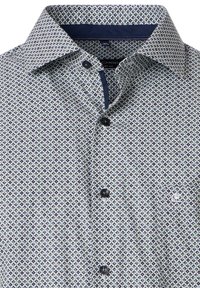 Wit en marineblauwe knoopshirt met een geometrisch ruitpatroon. Beschikt over een contrasterende kraag, zwarte knopen en een borstzak.