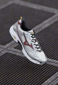 Grey and silver athletic sneaker with black accents, mesh texture, prominent red stripe design, and yellow logo on the heel.