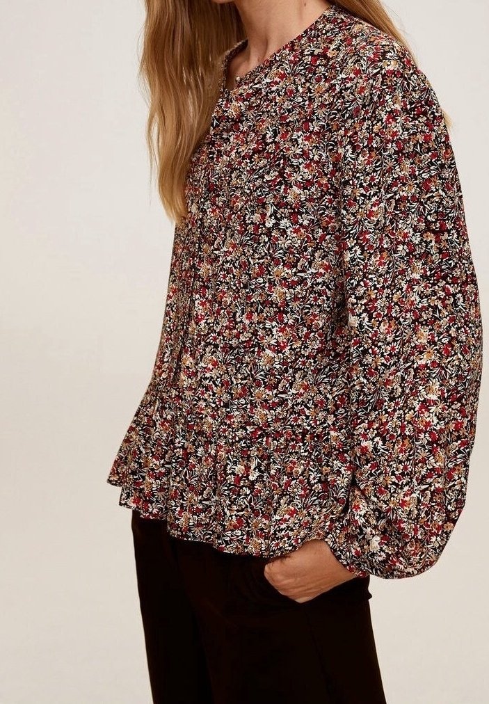 Floral blouse in zwart, met kleine rode, witte en gele bloemen. Heeft een geplooide zoom, ronde halslijn en lange pofmouwen.
