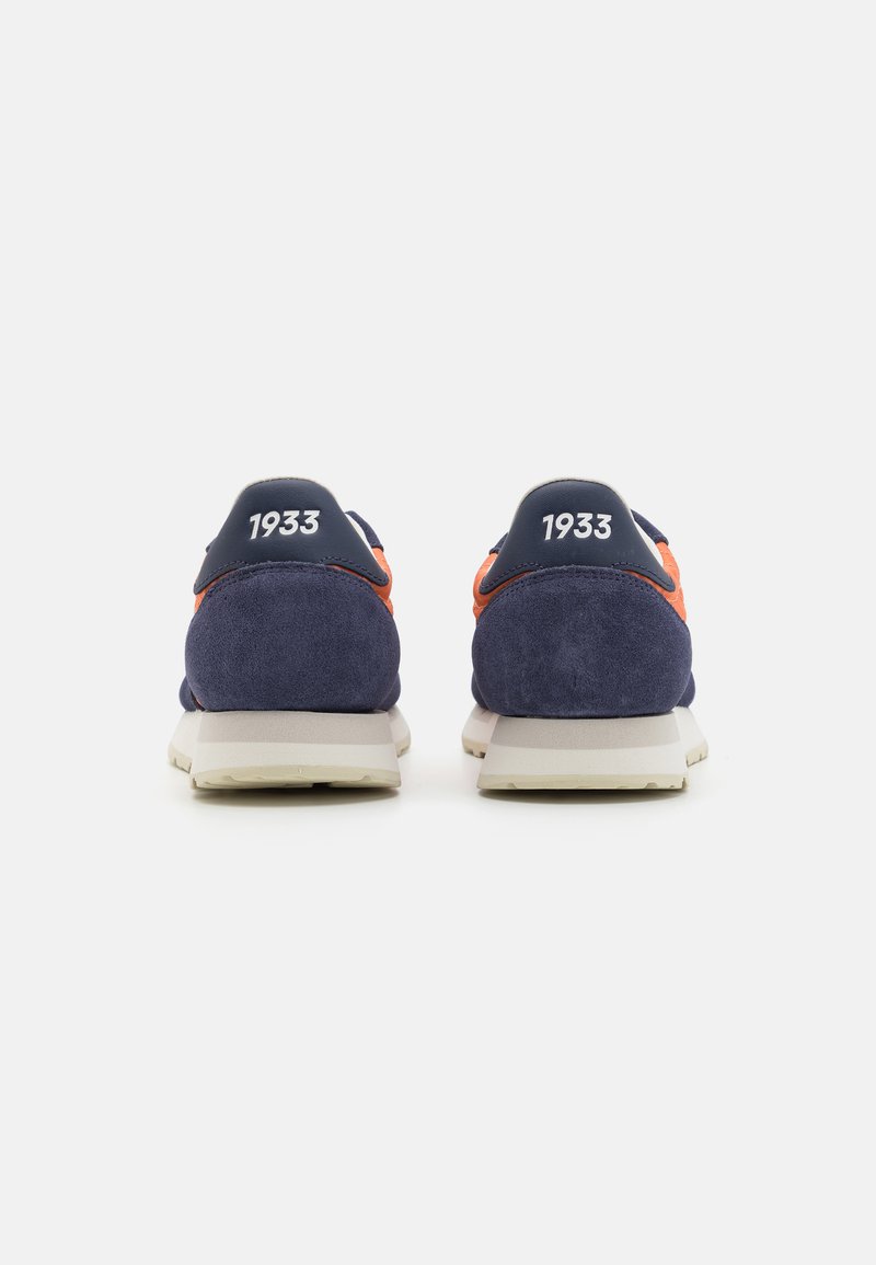 Zapatillas para hombre con parte superior de ante azul marino, acentos naranjas y suela de espuma blanca; presenta el número "1933" en el talón.