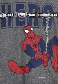 Graues T-Shirt mit Spider-Man in rot und blau, der ein Netz hält. "HERO" in großen blauen Buchstaben darüber gedruckt, mit grafischen Akzenten.