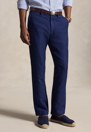 Homme portant un chino bleu, une ceinture en cuir marron, une chemise rayée bleu et blanc et des espadrilles bleu marine avec des semelles tressées.